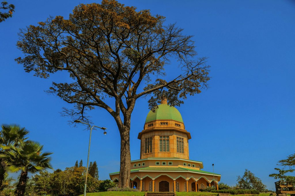 Stunning architecture of a religious building with a distinctive dome near a large tree against a clear blue sky.